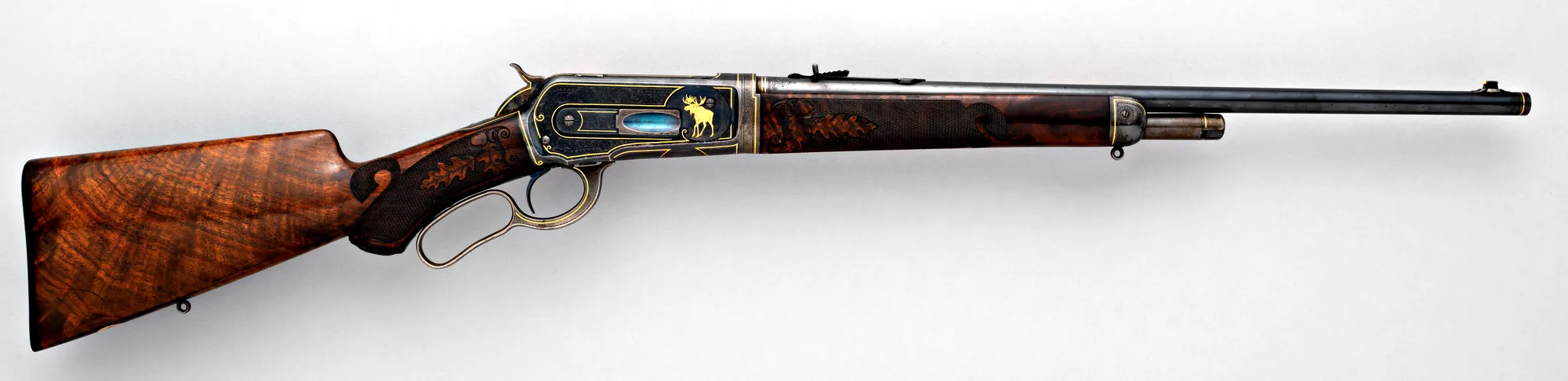 Winchester Model 1886 takedown rifle, right side: figured walnut stock, carved and checkered pistol grip, engraved receiver with a gold moose, and a half magazine ending short of the muzzle.