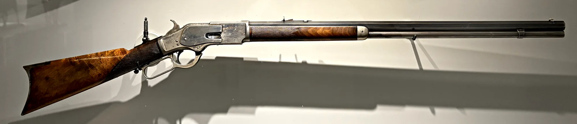 Winchester Model 1873 rifle, right side, full length: octagon barrel with visible flats, checkered forend and grip, tang peep sight behind the hammer, and a color case-hardened receiver.